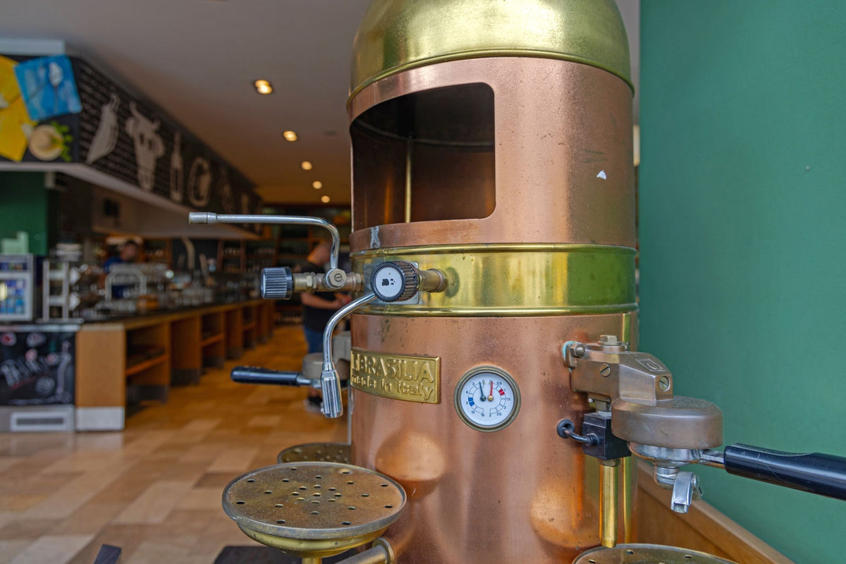 A vintage brass and copper lever espresso machine standing in a coffee shop