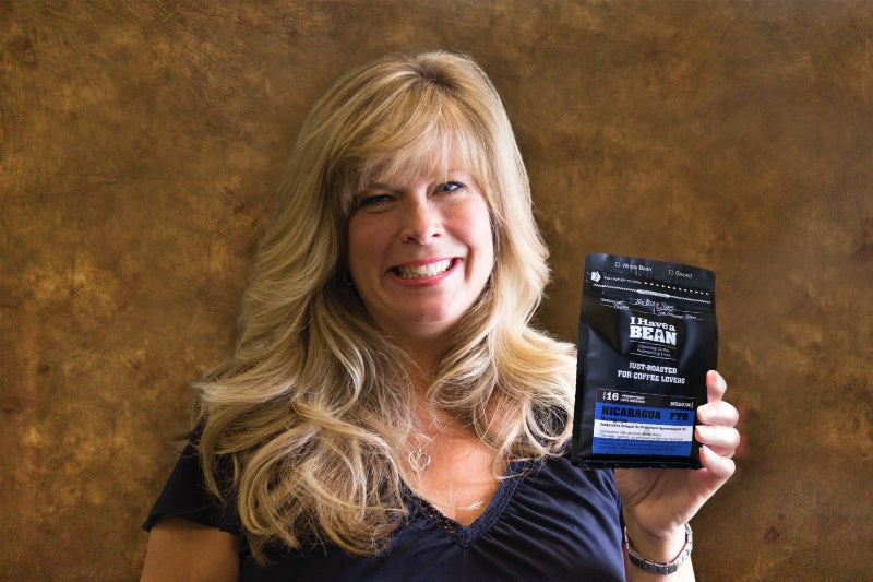 White woman standing in front of a brown background holding up a bag of I Have a Bean Nicaragua coffee