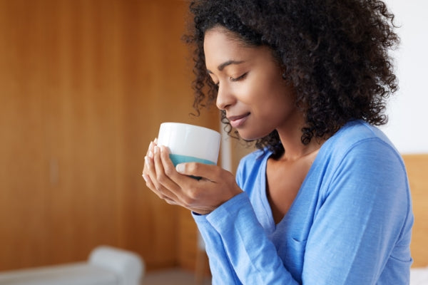 A Black woman in a blue shirt holding a coffee cup with her eyes closed