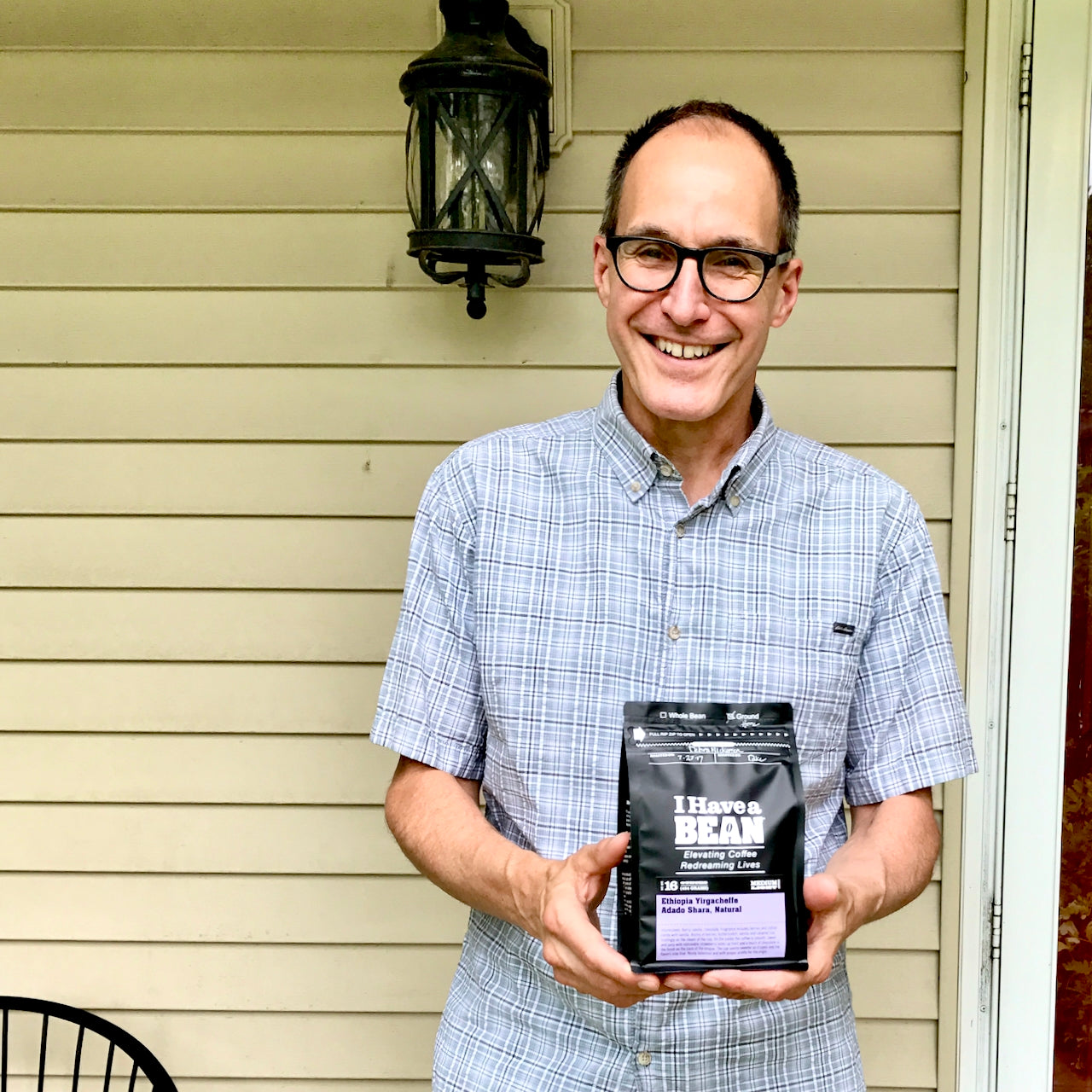 White man standing in front of a yellow wall holding a bag of I Have a Bean coffee