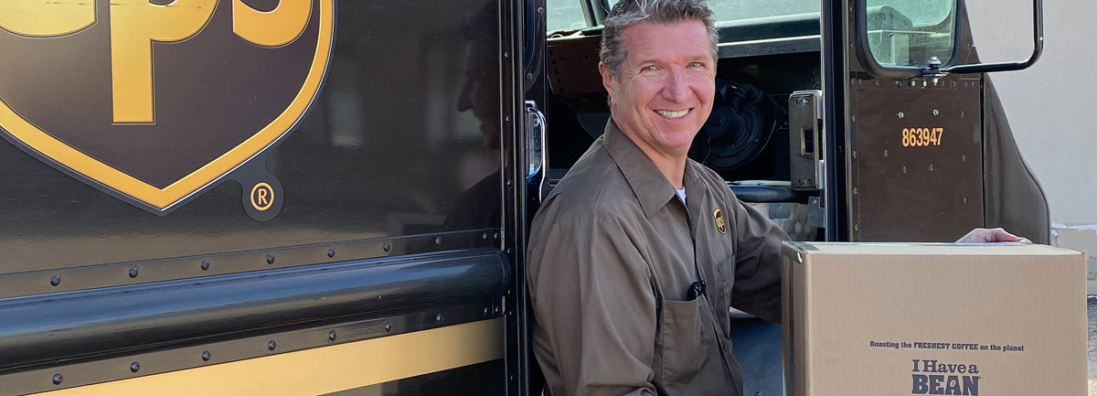 White man standing next to a UPS truck holding a brown box with the I Have a Bean logo on the side