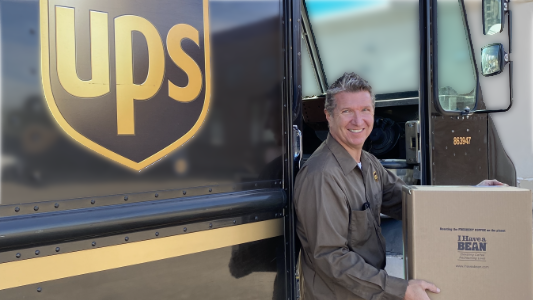 White man standing next to a UPS truck holding a brown box with the I Have a Bean logo on the side