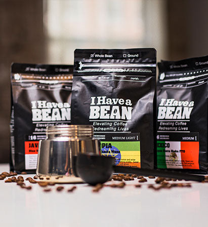three bags of i have a bean coffee beans with loose brown coffee beans and a silver jar in the foreground