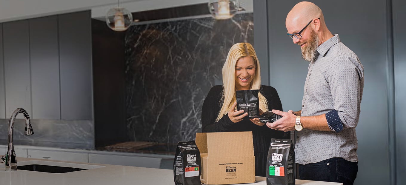 White man and woman both smiling and looking down at I Have a Bean coffee bags in their hands